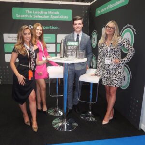 Four expert recruitment consultants from Aspion Search's team Metals stand around a table at the 2023 UK Metals Expo. 